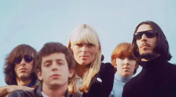 Cinco miembros de The Velvet Underground, pioneros del sonido new wave 80, posan con miradas intensas bajo un cielo azul.