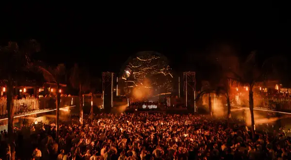 Multitud vibrante en el festival Sophie, disfrutando de la música bajo luces cálidas y palmeras.