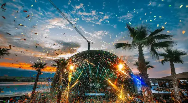 Multitud celebra en el festival croacia techno bajo confeti y luces. Palmeras y grúa completan la escena.