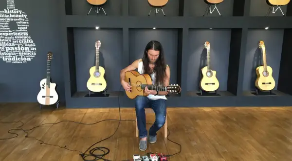 Un guitarrista con barba toca una guitarra acústica sentado frente a pedales de efectos.