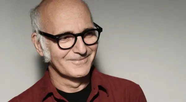 Retrato de Ludovico Einaudi, músico italiano. Su edad se refleja en su mirada serena y su cabello canoso. Viste una camisa roja.