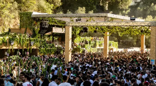 Multitud disfrutando de música electrónica en un evento al aire libre, con una estructura decorada con vegetación. Ambiente festivo en Brunch Electronik Lisboa.