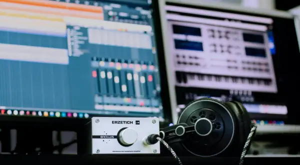 Estudio de **audio digital** con monitores mostrando software de producción musical, un amplificador de auriculares y auriculares negros.