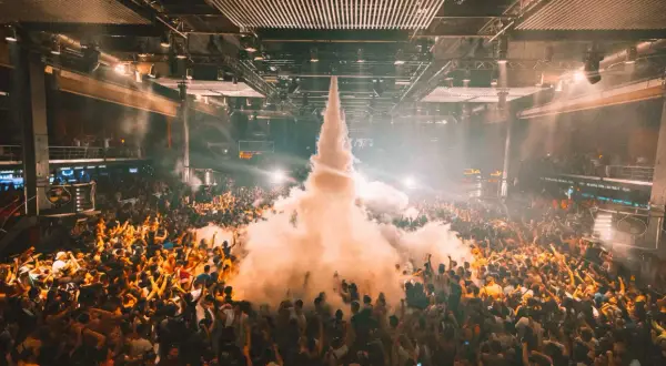 Multitud en un **tardeo techno Madrid**, con humo saliendo del centro y luces que iluminan la fiesta.