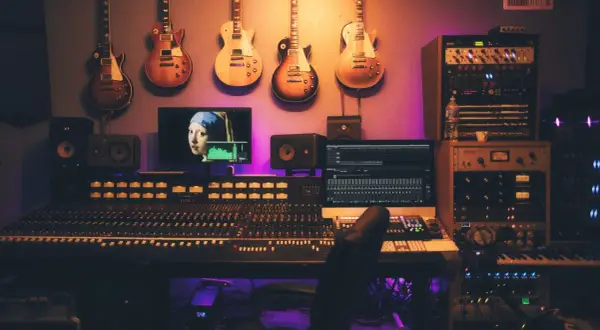 Estudio de grabación con guitarras colgadas, mesa de mezclas, monitores y un ordenador mostrando "La joven de la perla", ideal para samplear.