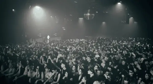 Multitud vibrante disfrutando de la techno musica en un club con luces tenues y una bola de discoteca giratoria.