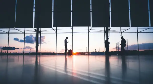 Siluetas de personas con maletas en un aeropuerto al atardecer. Quizás buscando ofertas en **que es ticketswap** para su próximo viaje.