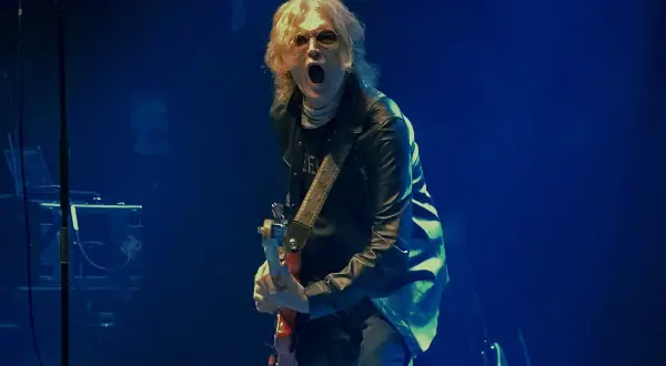 Glenn Hughes, con su banda, desata energía en el escenario. El vocalista y guitarrista, con su icónica melena rubia, grita al público mientras toca su instrumento.