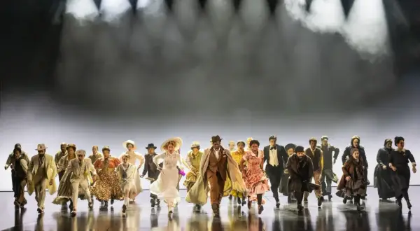 Un grupo diverso de personas corre hacia adelante en un escenario, evocando la energía y el espíritu de "Ragtime, que es".