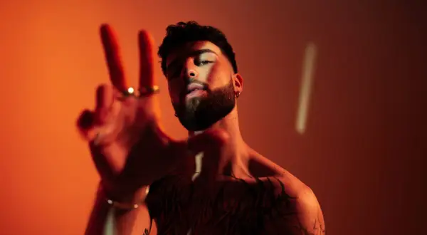 Joven con tatuajes y barba hace el signo de la paz. ¿Oguz DJ de dónde es?