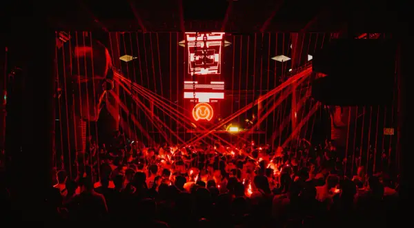 Multitud vibrante en un club nocturno, bañada en luces rojas. El logo de "Circus Nation" ilumina el escenario.