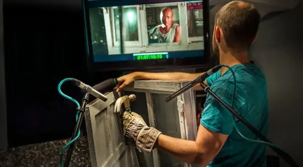 Un técnico de sonido crea efectos de **foley que es** el arte de añadir sonidos a una película, golpeando una ventana con un martillo.