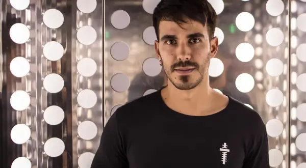 Raúl Pacheco DJ, con su mirada intensa, posa frente a un fondo metálico con círculos luminosos.