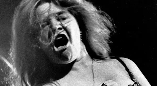 Janis Joplin canta con pasión, su boca abierta y cabello al viento capturan la energía cruda de su voz.