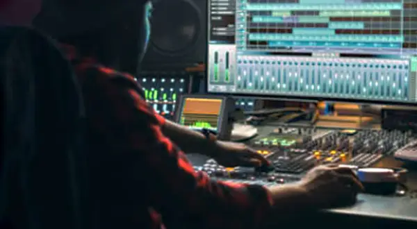 Persona trabajando en una mesa de mezclas, con una pantalla mostrando pistas de audio. Ideal para masterización online gratis.