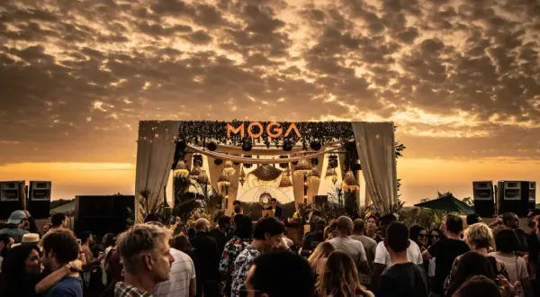 Multitud disfrutando del atardecer en el moga festival, con luces y escenario decorado.