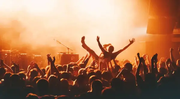 Multitud animada en un concierto, con una persona siendo levantada. La atmósfera naranja sugiere la emoción de los festivales en octubre.