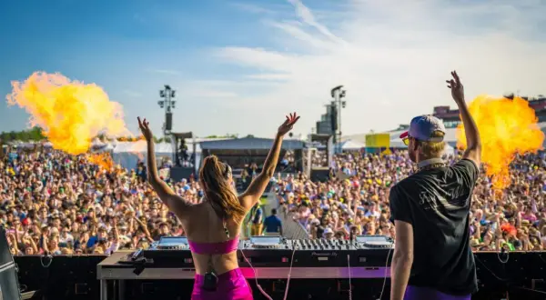 Dos DJs en un escenario lanzan fuego al aire ante una multitud masiva en uno de los festivales techno de Europa.