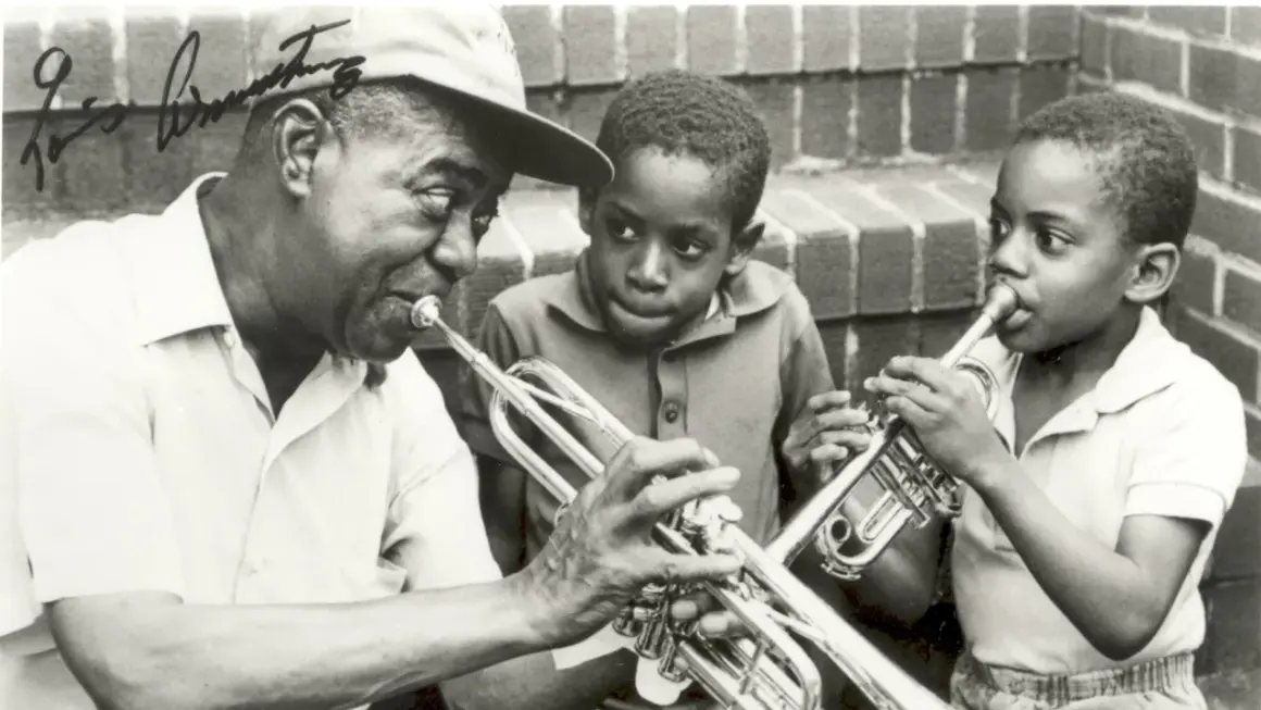 Louis Armstrong enseña a dos niños a tocar la trompeta. Ella Fitzgerald, aunque no está en la imagen, es una leyenda del jazz junto a él.