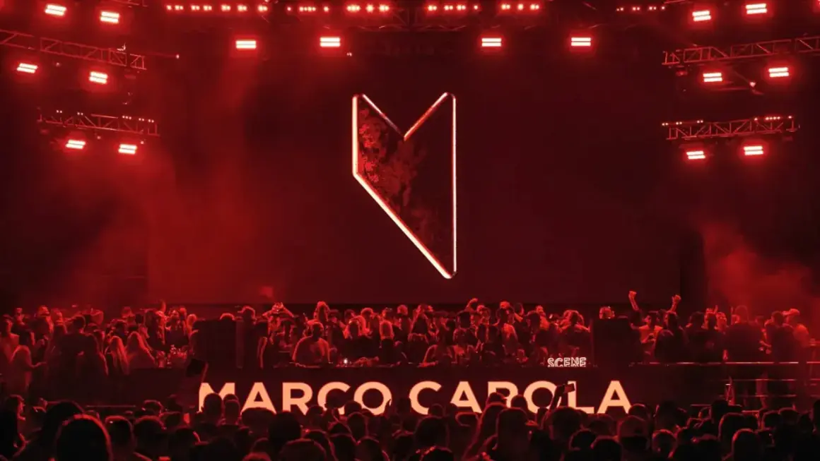 Multitud vibrante en Madrid, luces rojas y el logo de Marco Carola iluminan la noche.