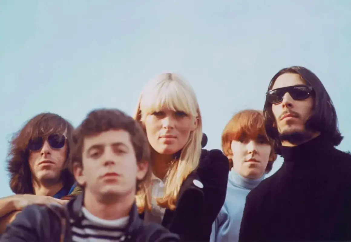 Cinco miembros de The Velvet Underground, pioneros del sonido new wave 80, posan con miradas intensas bajo un cielo azul.