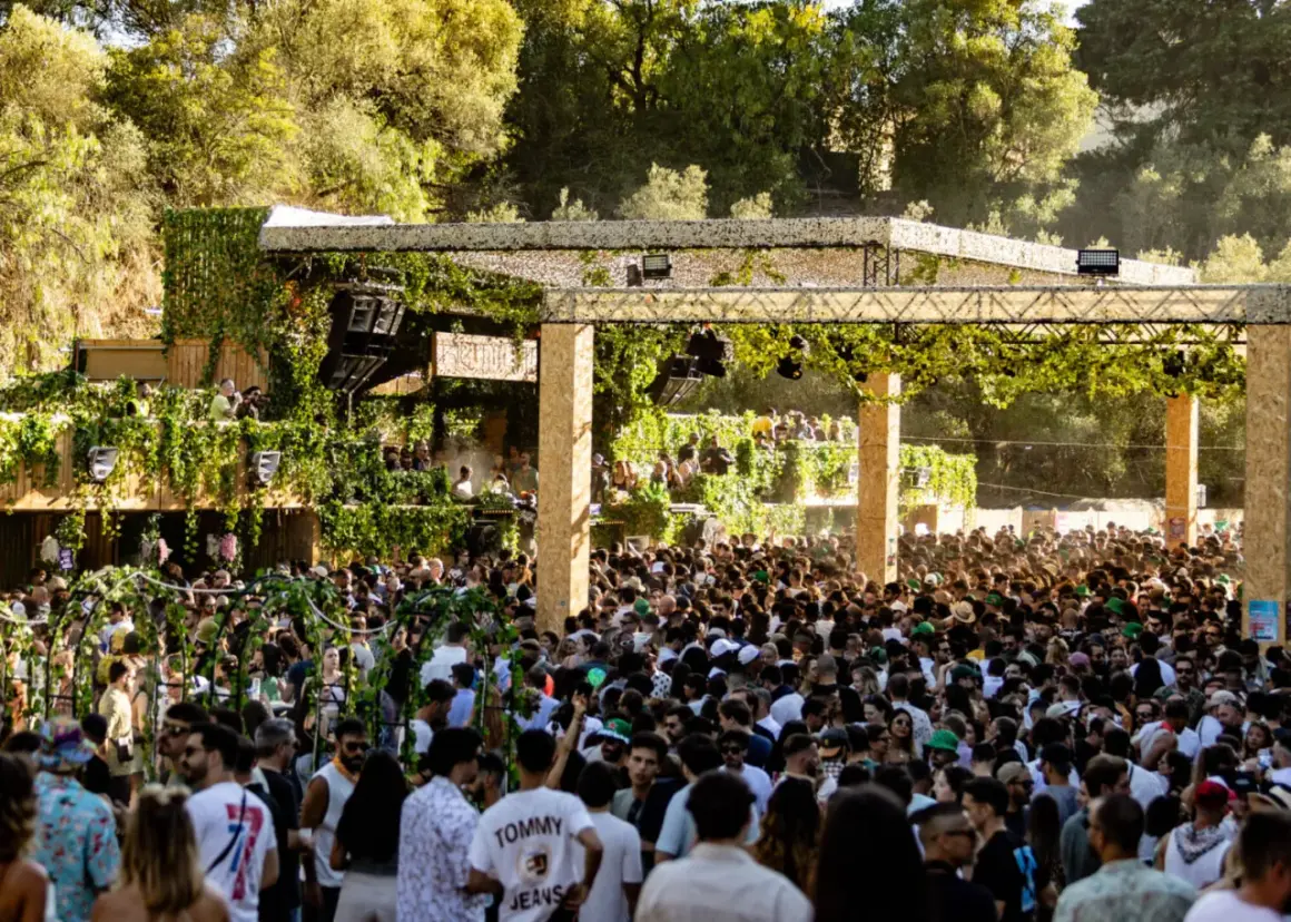 Multitud disfrutando de música electrónica en un evento al aire libre, con una estructura decorada con vegetación. Ambiente festivo en Brunch Electronik Lisboa.