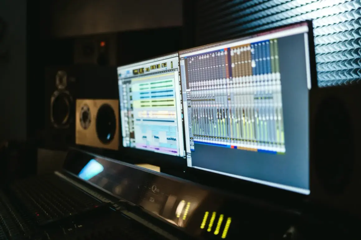 Monitores con software de producción electrónica y mesa de mezclas en un estudio de sonido.
