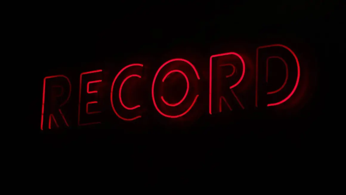 Letrero de neón rojo con la palabra "RECORD", evocando la era dorada de los sellos discográficos y la música.