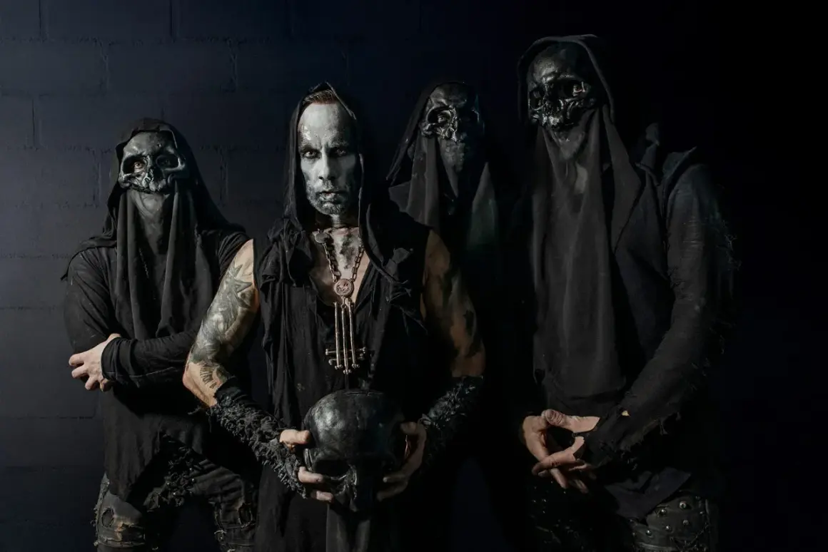 Cuatro figuras encapuchadas, con máscaras de calavera y maquillaje facial pálido, posan sombríamente. El líder sostiene un cráneo, evocando la estética de grupos black metal.