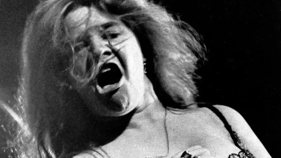 Janis Joplin canta con pasión, su boca abierta y cabello al viento capturan la energía cruda de su voz.