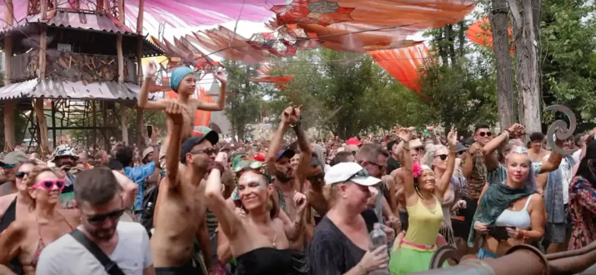 Multitud bailando en un festival psytrance España, con decoraciones coloridas y una estructura de madera.