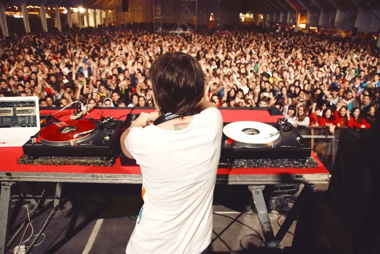 DJ en acci&oacute;n ante una multitud euf&oacute;rica, demostrando como ser un buen dj mezclando m&uacute;sica.