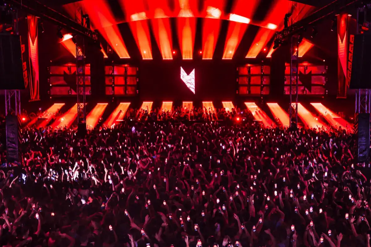 Multitud en concierto con luces rojas y logo en pantalla. Marco Carola en Madrid, creando una noche inolvidable.