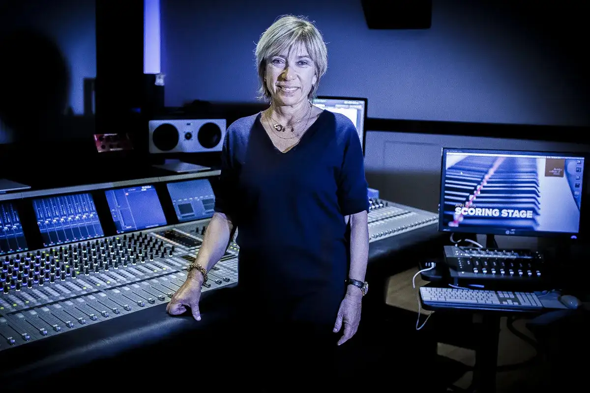 Una manager de cantantes sonríe en un estudio de grabación, rodeada de consolas de sonido y pantallas.