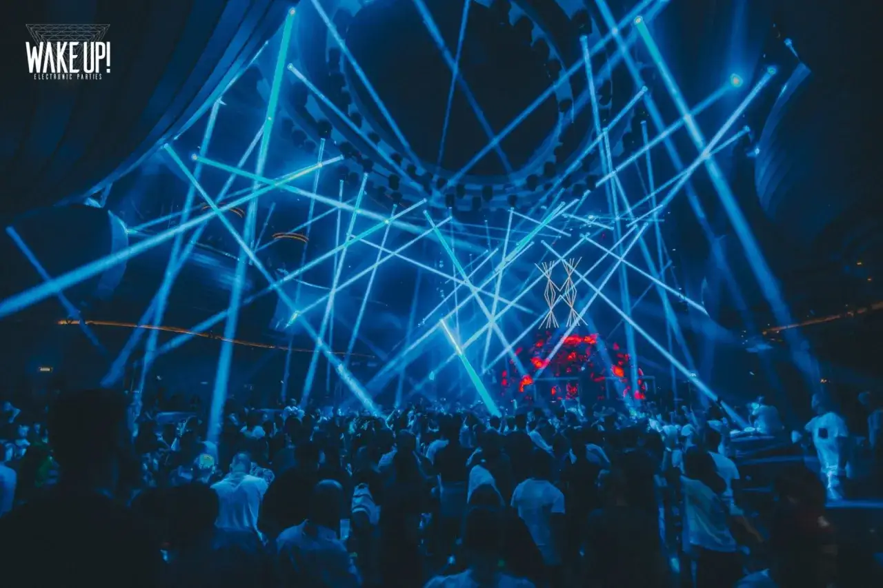 Una multitud baila bajo un espect&aacute;culo de luces azules en un evento de m&uacute;sica electr&oacute;nica. El logo 