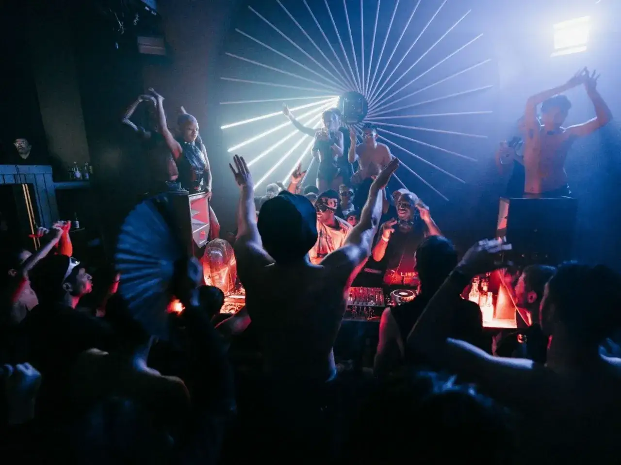 Gente bailando en una fiesta con luces de neón y un DJ. La atmósfera es eléctrica, como si todos supieran como entrar en Berghain.