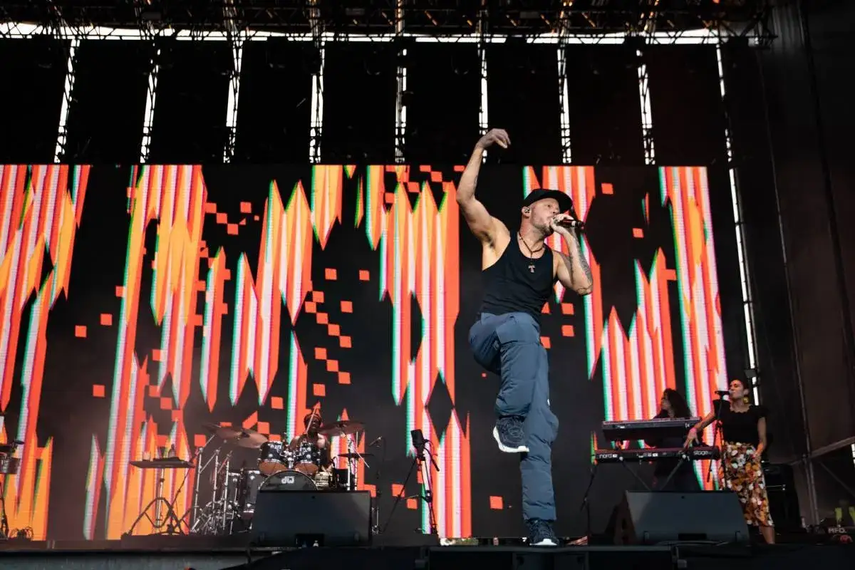 Residente en pleno concierto en Espa&ntilde;a, con un fondo de luces vibrantes y un baterista en acci&oacute;n.