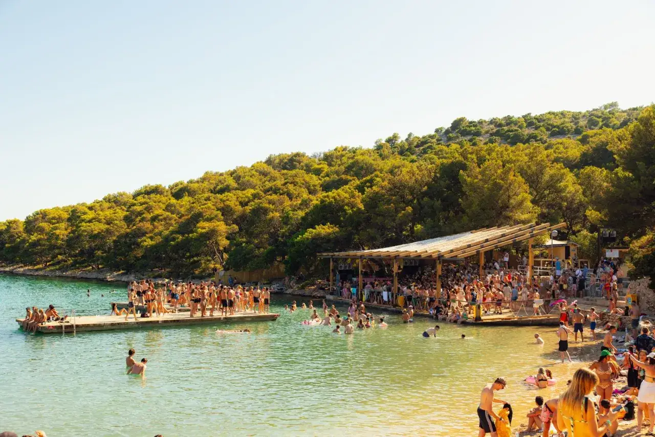 Gente disfrutando en un festival croacia techno junto al mar, con música y baile en la playa y en el agua.