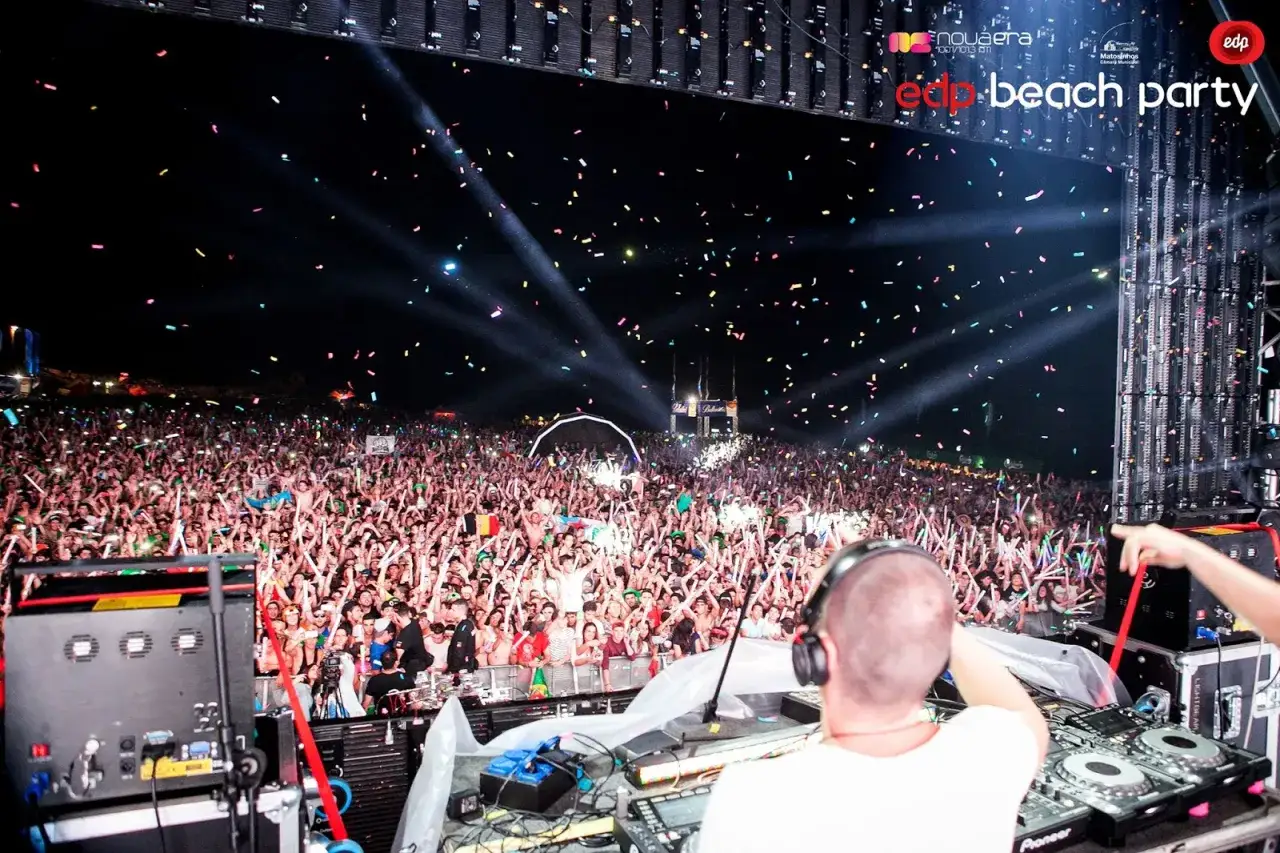Multitud vibrante en la edp beach party, con confeti cayendo y luces iluminando la noche.