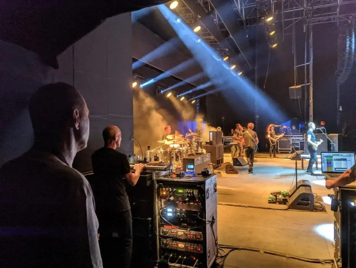Un promotor supervisa la banda en el escenario, con luces y humo creando un ambiente de concierto.