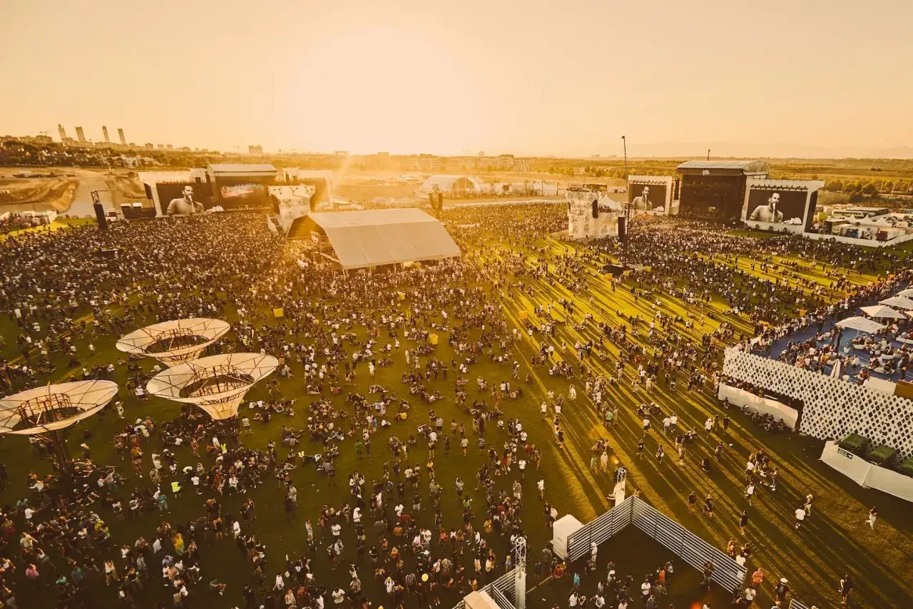 Gran multitud disfrutando de un concierto al atardecer. Las pantallas gigantes muestran al artista, creando una experiencia de iberdrola music inolvidable.