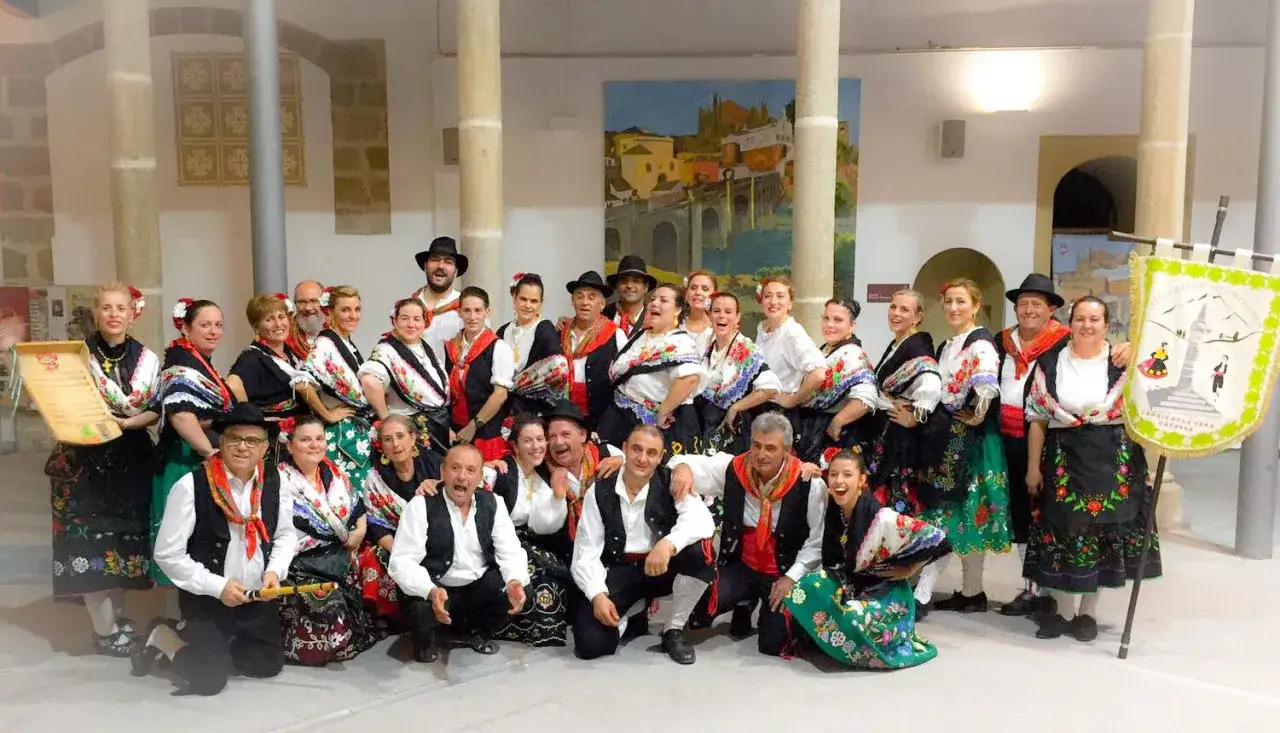 Grupo posa con trajes típicos, celebrando la historia del folklore extremeño. Llevan bordados coloridos y pañuelos, reflejando la rica cultura de la región.