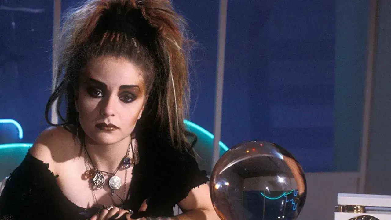 Chica con maquillaje dram&aacute;tico y peinado voluminoso, evocando la est&eacute;tica de la new wave music, junto a una esfera de cristal.