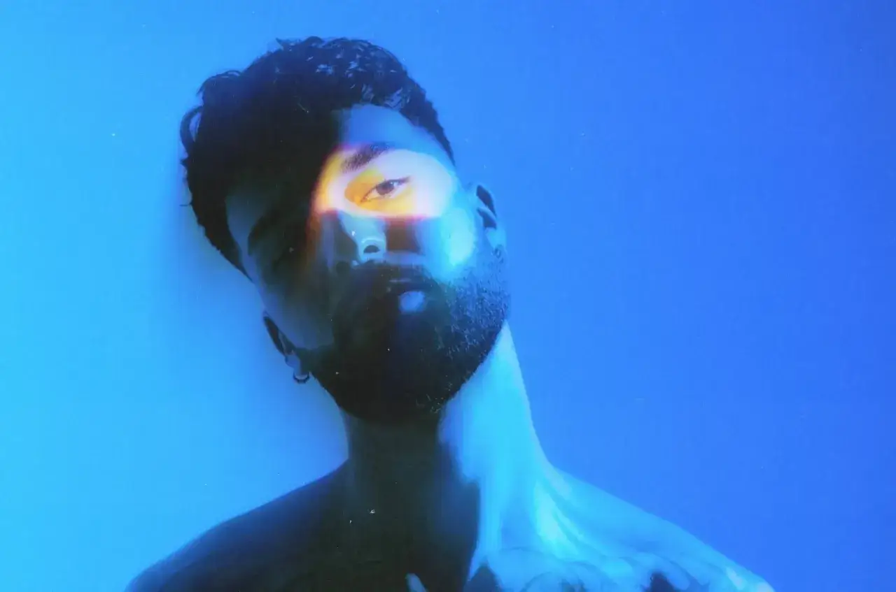 Oğuz DJ, ¿de dónde es? Un primer plano de su rostro con iluminación azul y un rayo de luz amarilla sobre su ojo.