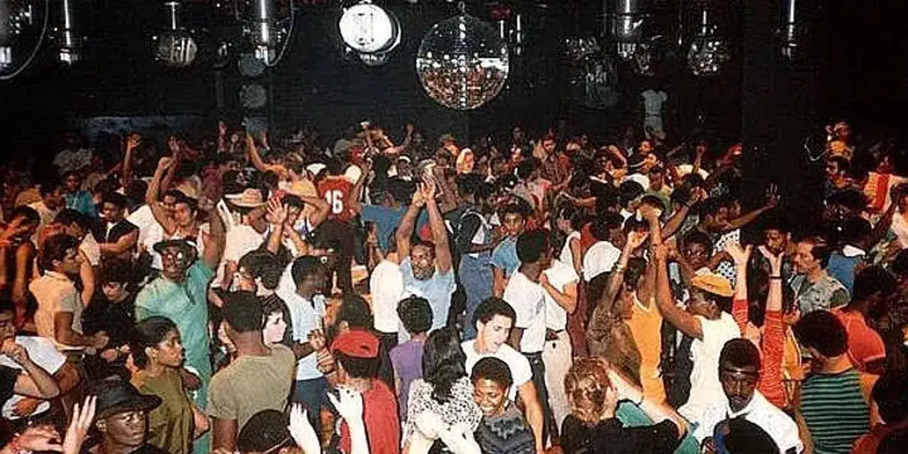 Una multitud baila en una discoteca, con luces de bola de espejos y un ambiente vibrante, evocando el espíritu del house, el género musical.