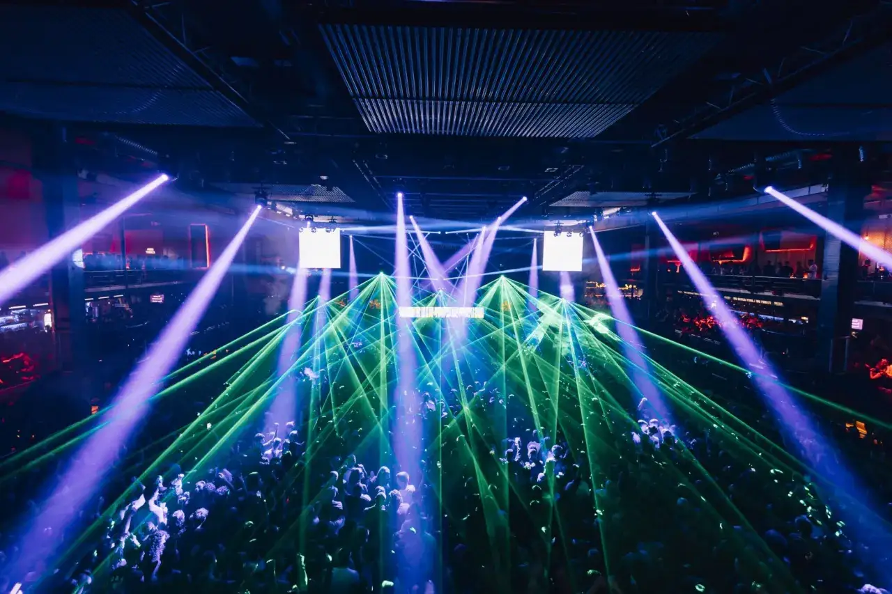 Una multitud baila bajo luces láser verdes y moradas en una discoteca. El evento, con el código 11 octubre, crea una atmósfera vibrante.