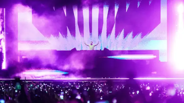DJ en escenario con luces moradas y público con móviles. Un momento cumbre de la industria de la música.