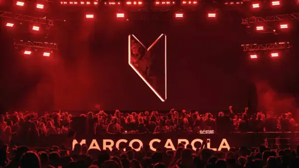 Multitud vibrante en Madrid, luces rojas y el logo de Marco Carola iluminan la noche.