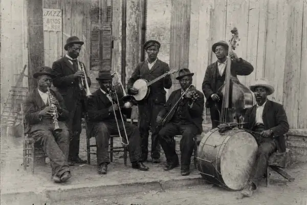 Grupo de músicos tocando jazz años 50: clarinete, trombón, banjo, violín, contrabajo y batería.