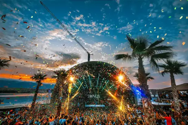 Multitud celebra en el festival croacia techno bajo confeti y luces. Palmeras y grúa completan la escena.